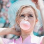 Photo of blond haired girl blowing pink bubble gum.