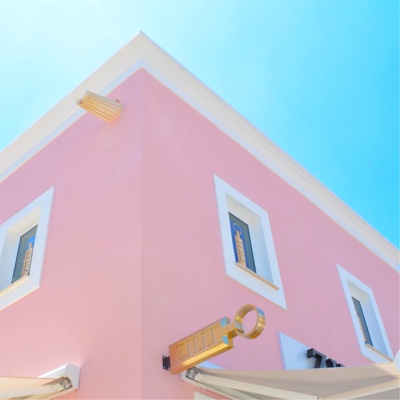 View of top half of a pink house with white trimmed windows, againste a bright blue sky.